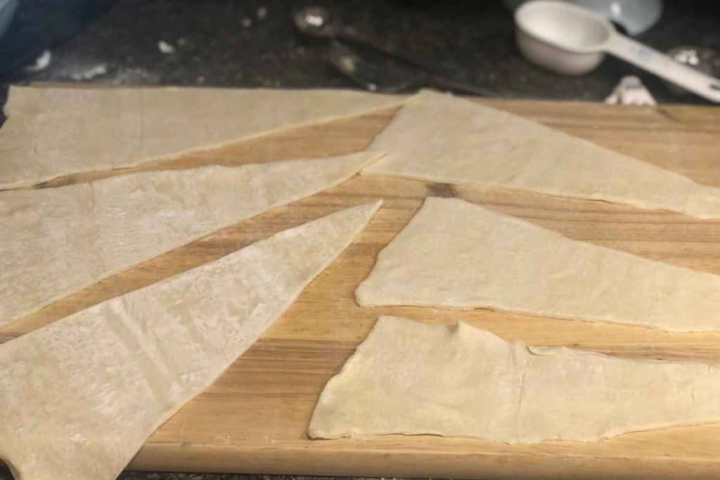 Puff pastry rolled out and cut into triangle shapes to be turned into almond croissants