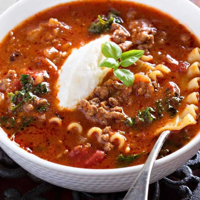Bowl of lasagna soup with a cheese mixture garnish in a white bowl and spoon