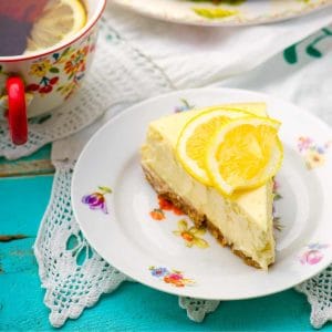 Slice of no-bake lemonade cheesecake plated on a flowery plate with lemon slices on top