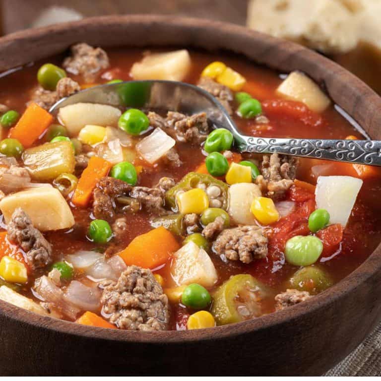 Wooden soup bowl filled with Easy and Quick Instant Pot Vegetable Beef Soup Recipe with a silver spoon.