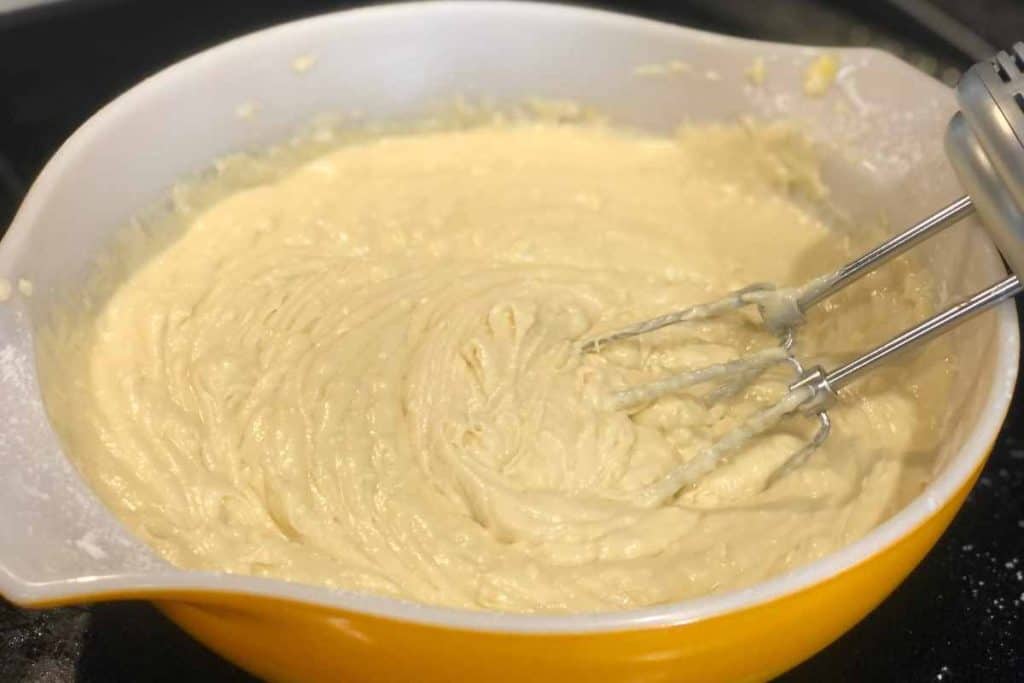The batter for Blueberry Lemon Loaf in an orange bowl with an electric mixer.