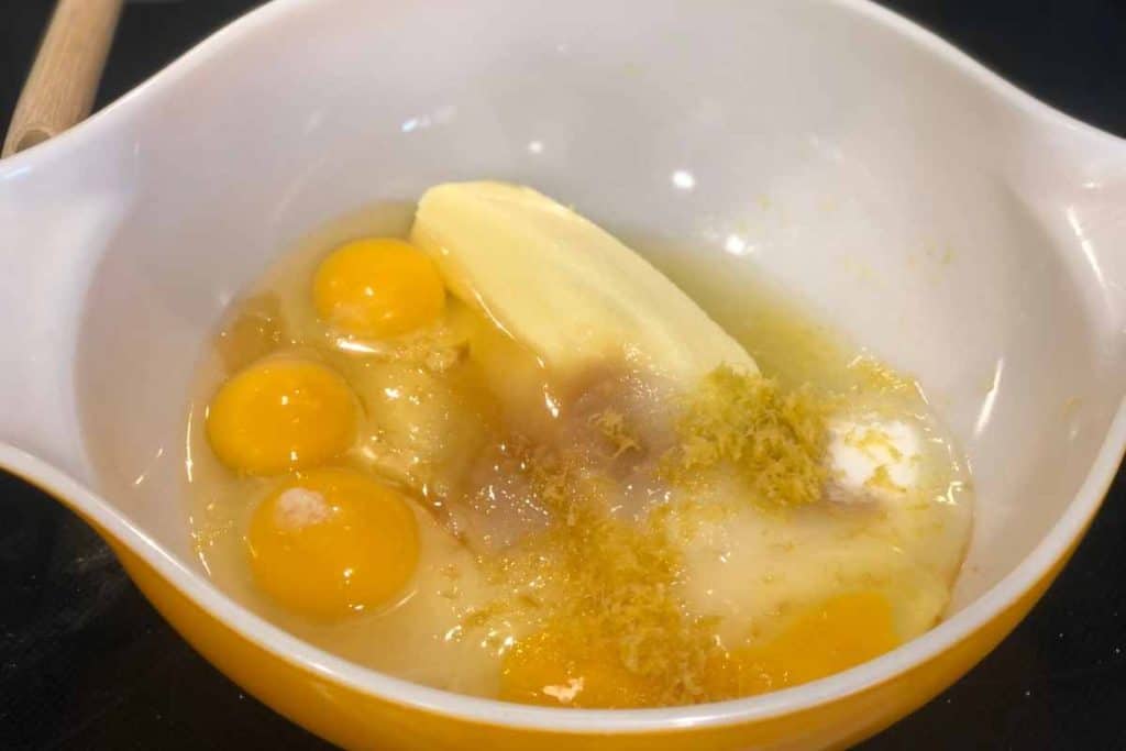 An orange mixing bowl with the wet ingredients for Blueberry Lemon Loaf including eggs, sugar and butter along with lemon zest.