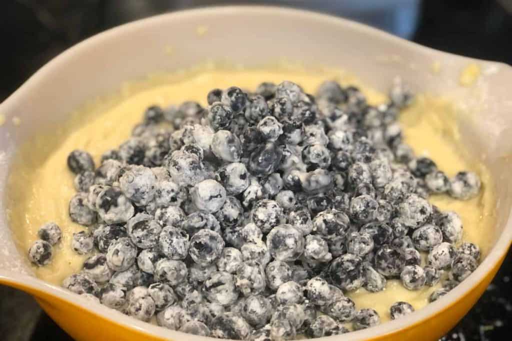 Blueberries tossed and coated with flour on top of the batter for Blueberry Lemon Loaf in an orange mixing bowl