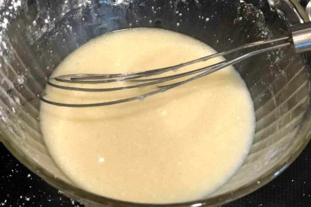 Lemon glaze with a whisk in it in a glass mixing bowl for the topping for Blueberry Lemon Loaf