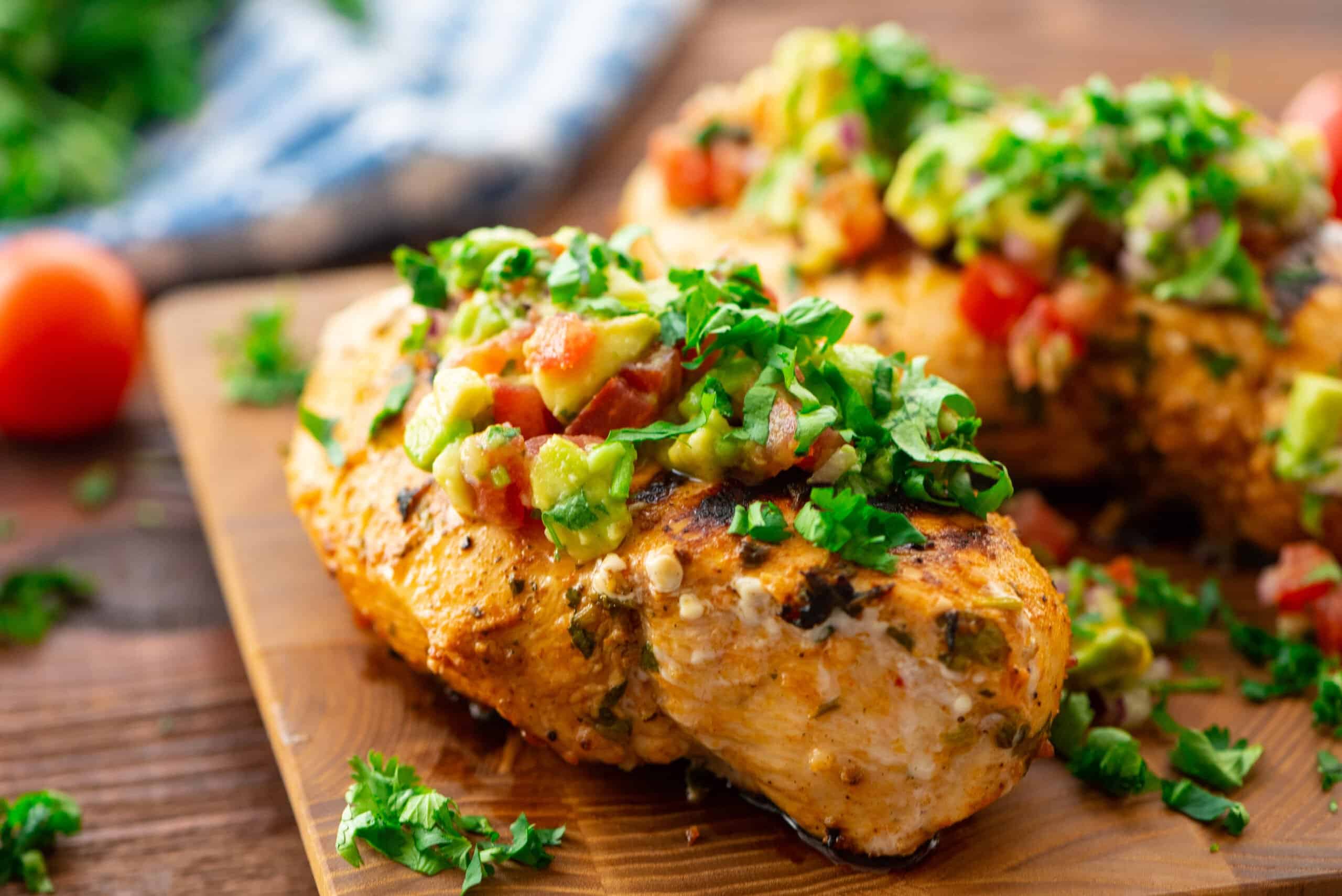 Cilantro Lime Grilled Chicken on a wooden cutting board with tomatoes and avocados and cilantro topping