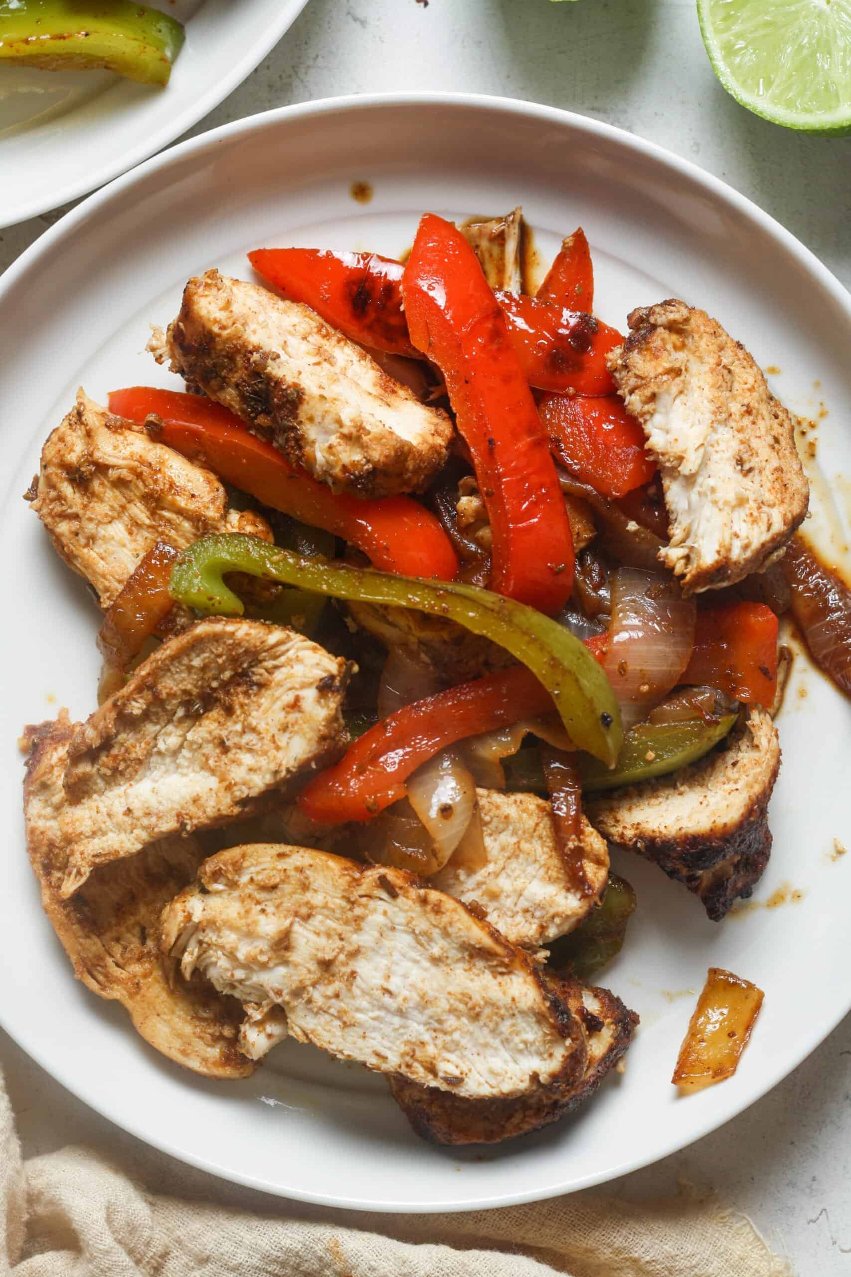 Chicken Fajitas on a white plate on a table with limes and peppers