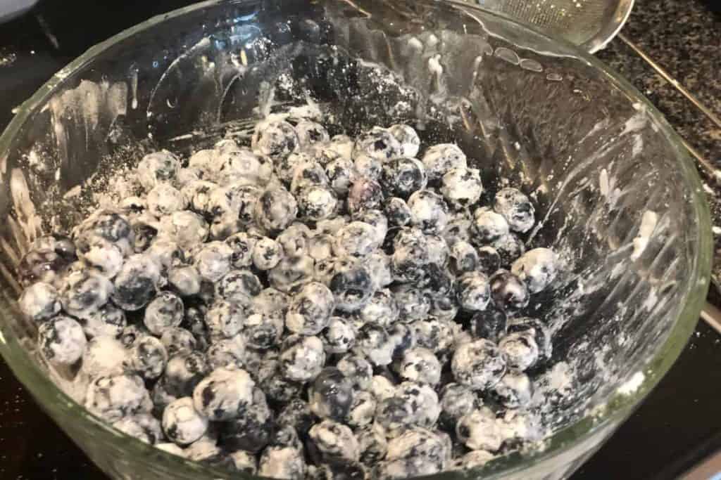 Blueberries in a glass mixing bowl coated with flour