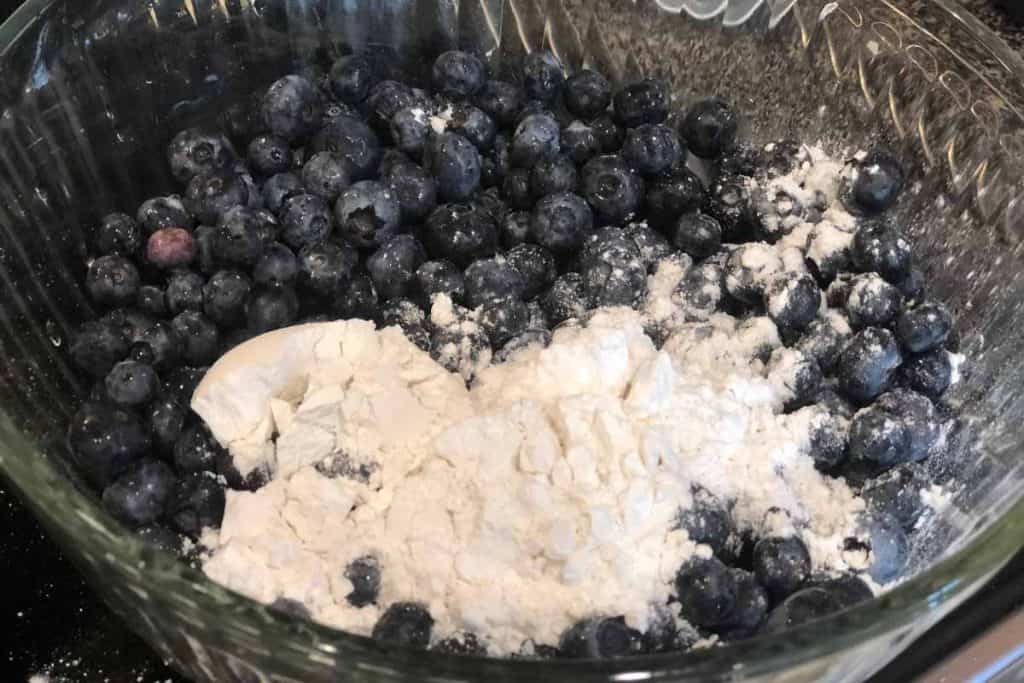 Blueberries in a glass bowl with flour dumped on top ready to be mixed together