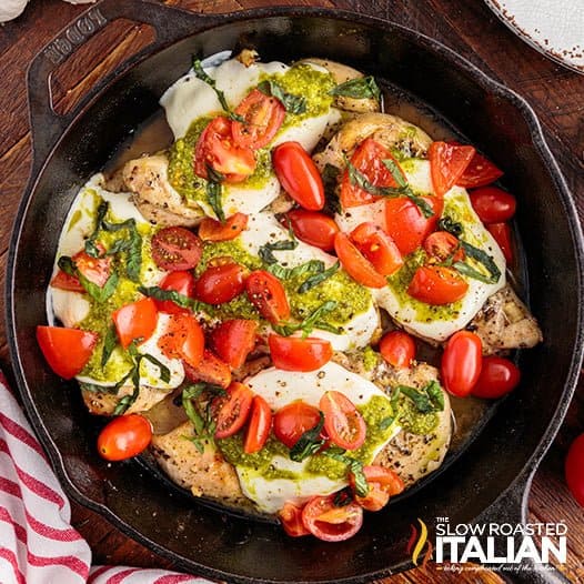 Cast iron skillet with Grilled Chicken Margherita Olive Garden Copycat recipe, covered in tomatoes and pesto