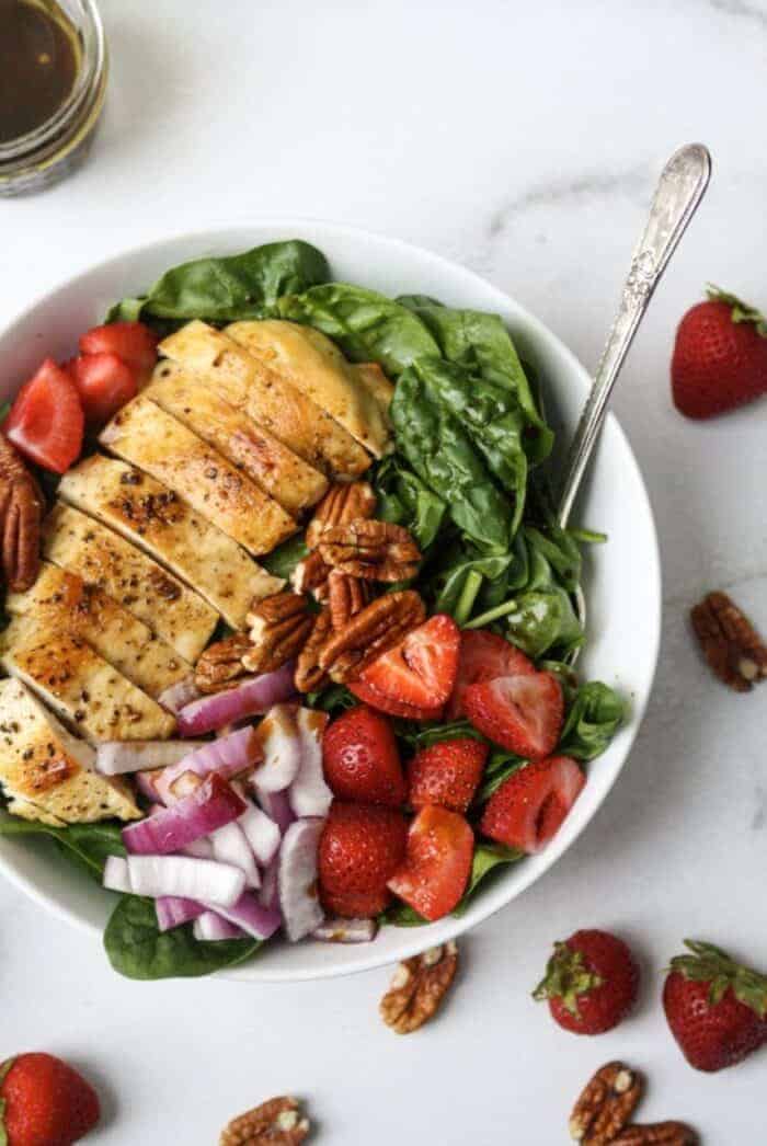 Whole30 Grilled Chicken Strawberry Salad with chicken, strawberreis, red onions and pecans in a white bowl.