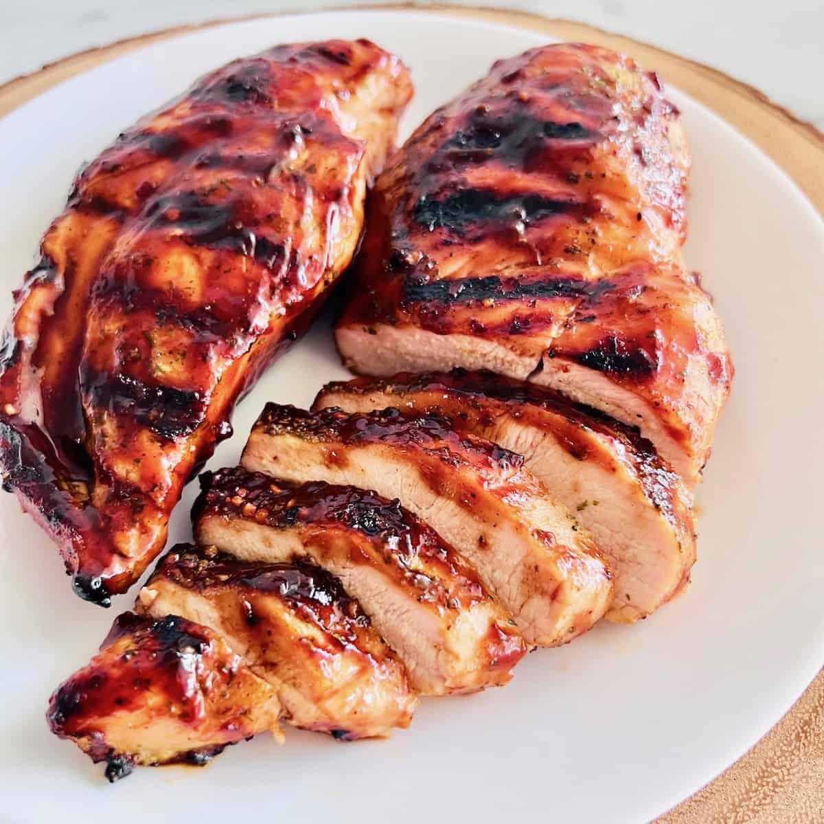 Grilled BBQ Chicken Breasts partially sliced up on a white plate