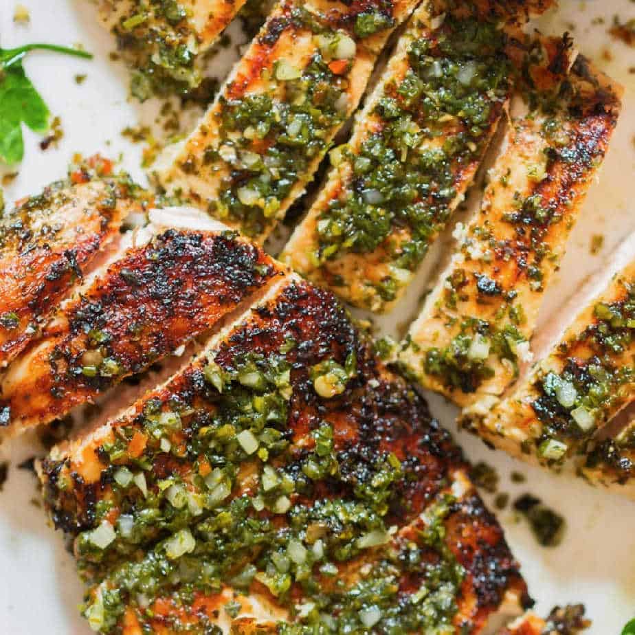 Grilled Chimichurri Chicken sliced on a cutting board with a chimicurri sauce on top.