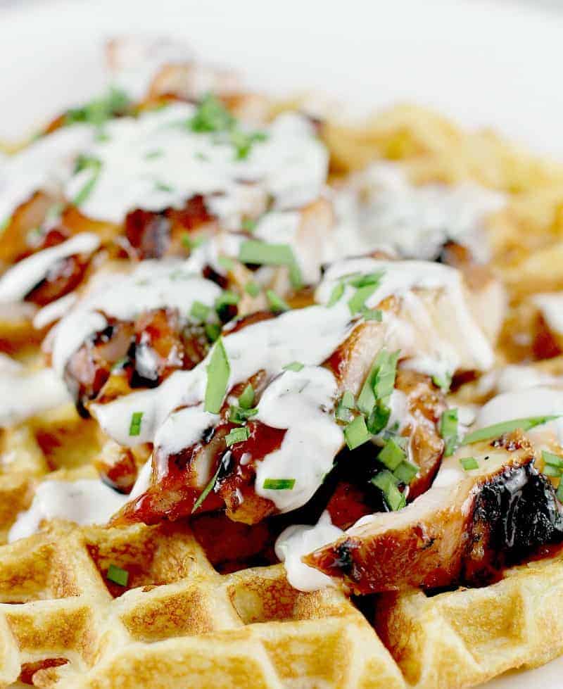 Honey Beer BBQ Chicken and Waffles recipe has a waffle with sliced grilled chicken on top with a white cream sauce drizzled all over the chicken.