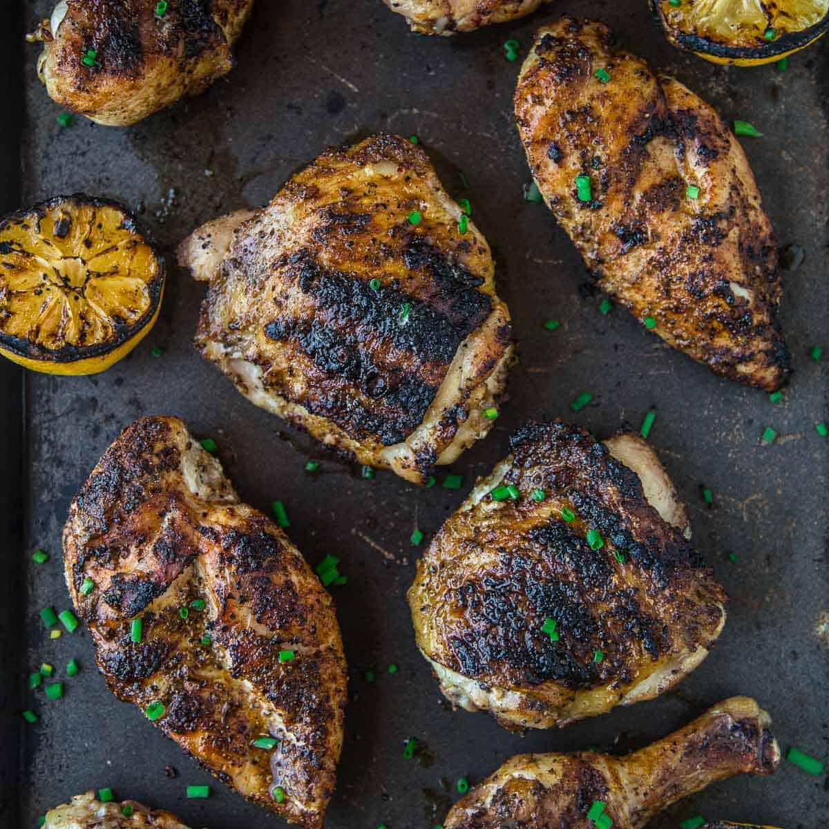 Grilled chicken on a black platter with great char marks and grilled lemons on the platter