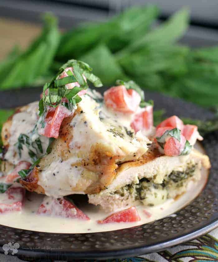 This recipe is Pesto Chicken with Basil Tomato Cream and has sliced grilled chicken on a plate covered in tomatoes and pesto sauce with fresh basil sprinkled on top