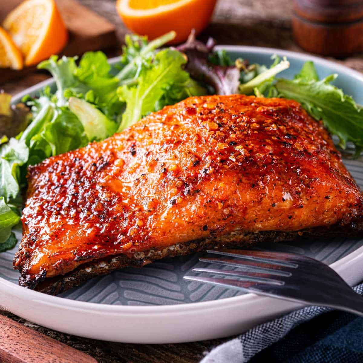 Honey Teriyaki Glazed Salmon on a plate with a green salad next to it and a fork