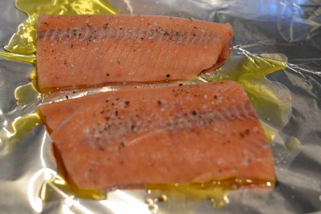 Two salmon filets seasoned with salt and pepper with a little bit of olive oil on aluminum foil