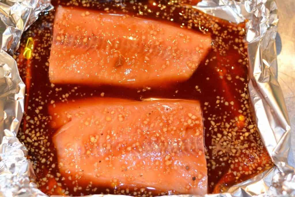 Raw salmon in a foil packet with a honey teriyaki glaze poured on top of the fish.