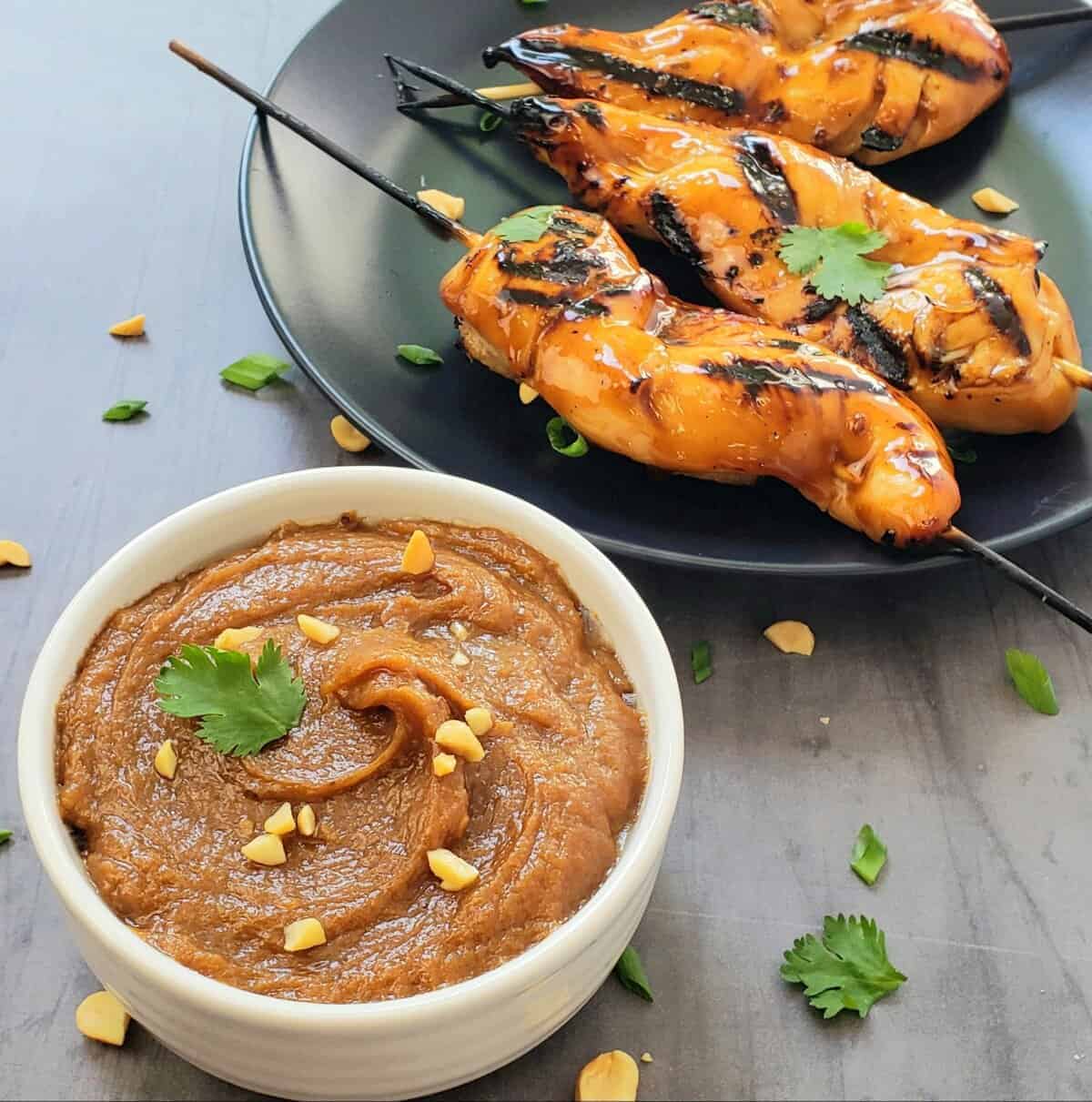 Shortcut Teriyaki Grilled Chicken Tenders on a black plate with a dish of spicy peanut sauce on the side.