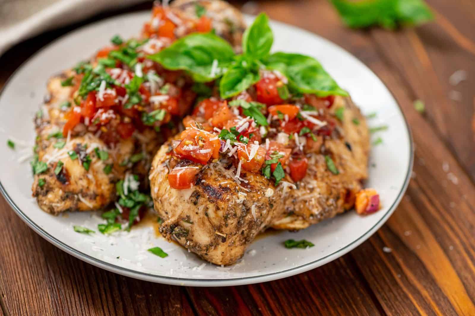 Grilled Bruschetta Chicken on a white plate on a wooden table, topped with a fresh sprig of basil.
