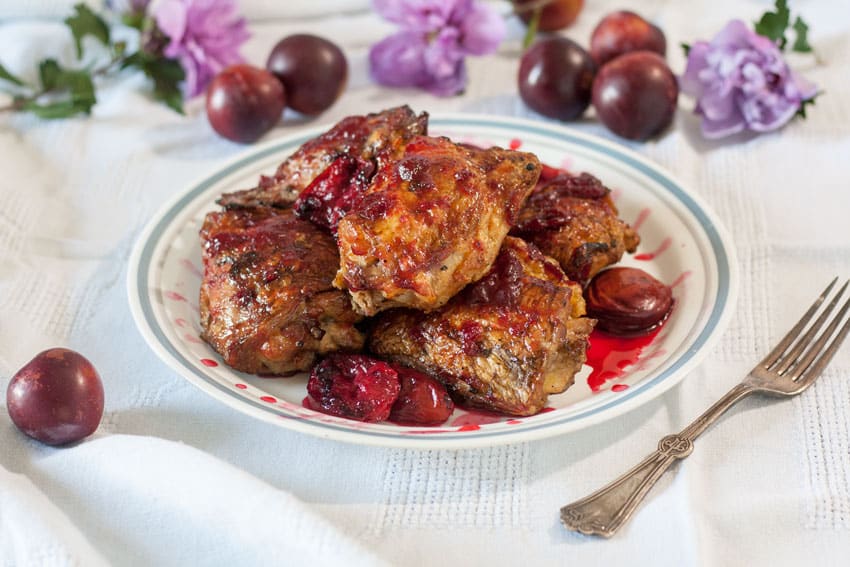 Chicken with Plum Sauce and Grilled Plums on a white plate and a white tablecloth and plums.