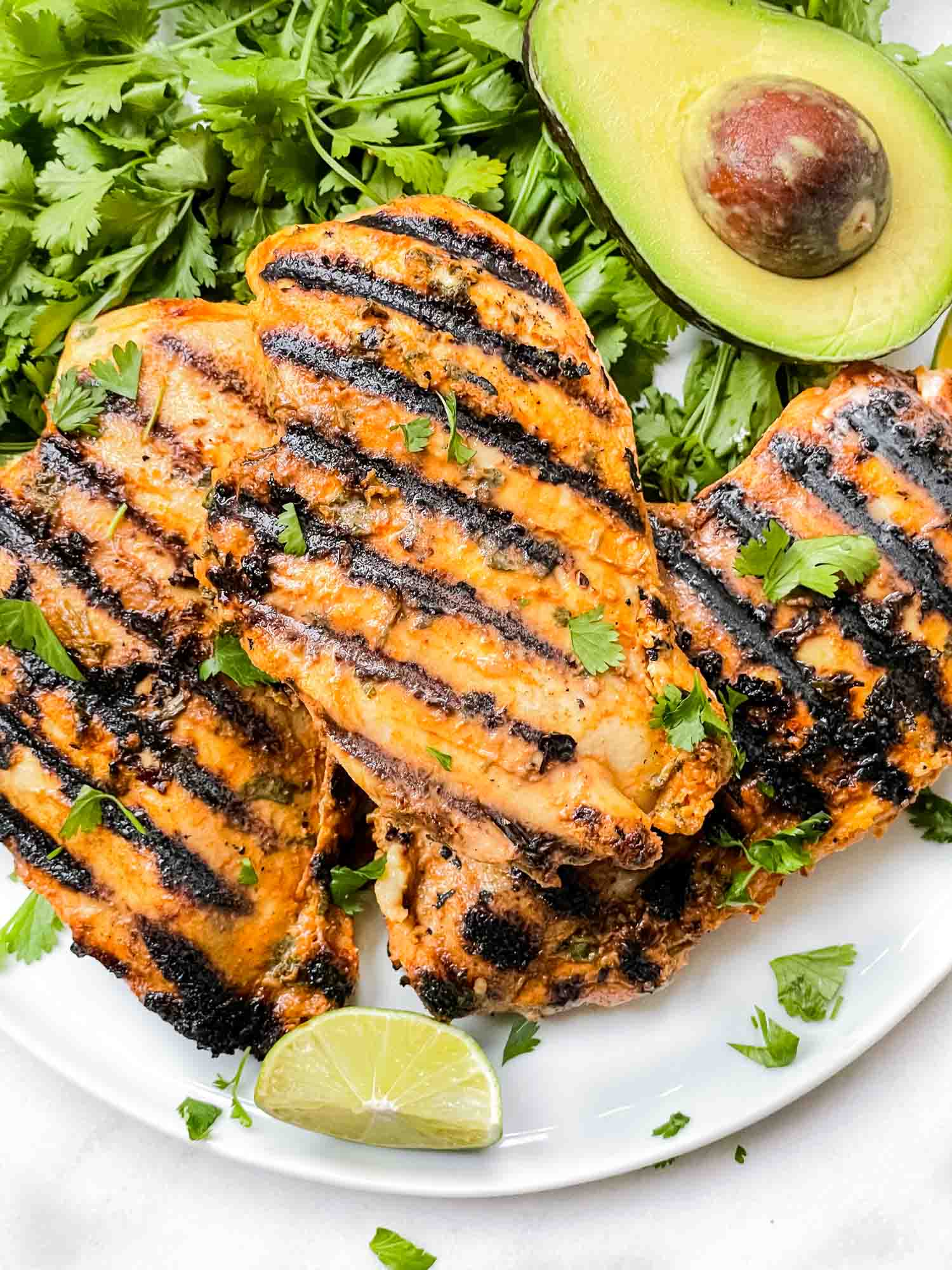 Cilantro Lime Grilled Chicken on a white plate with fresh avocado, limes and cilantro.