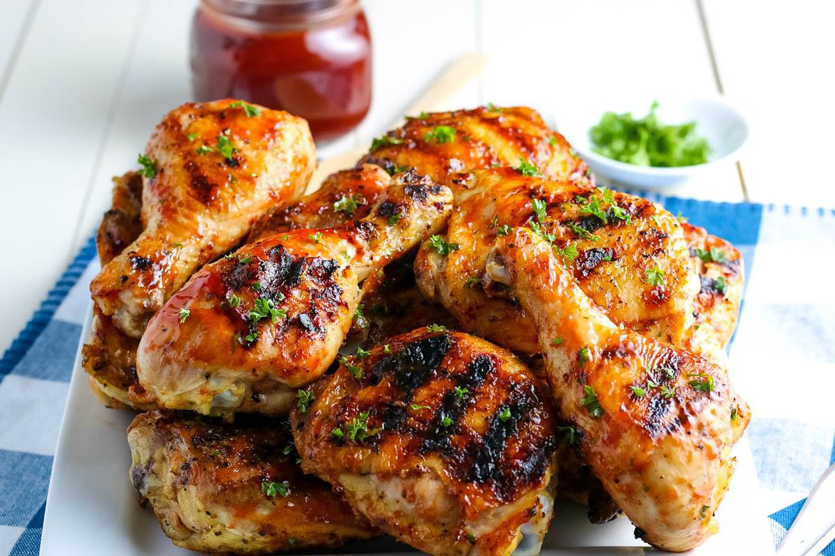 Easy Grilled BBQ Chicken piled up on a white plate with bbq on the side on a white table.