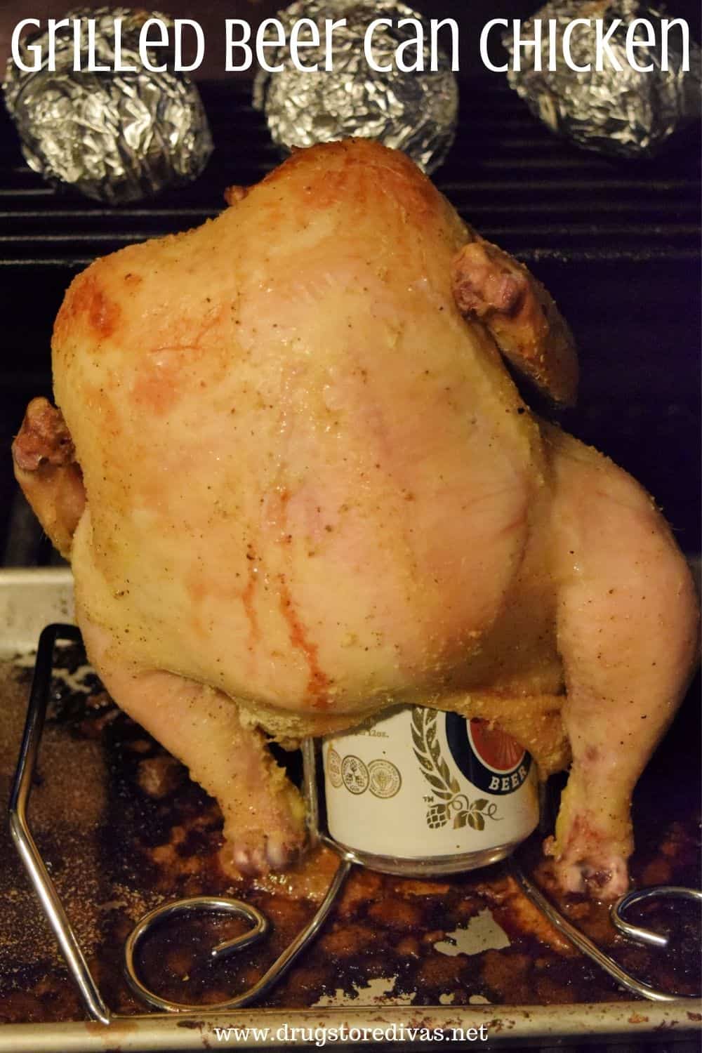 A whole chicken sitting upright on a beer can in a pan on the grill.