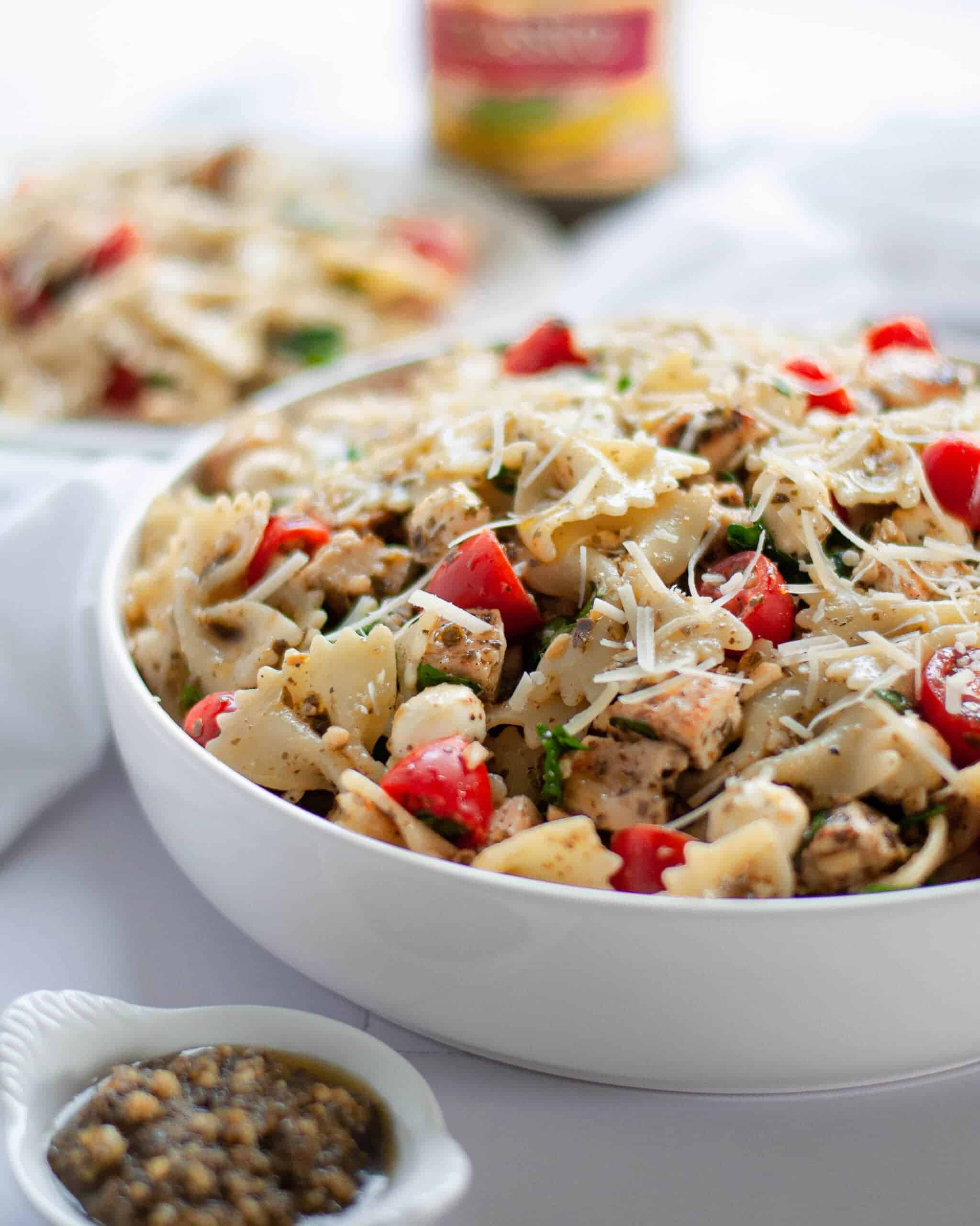 Pesto Pasta Salad with Chicken in a white bowl on a white tablecloth covered table.