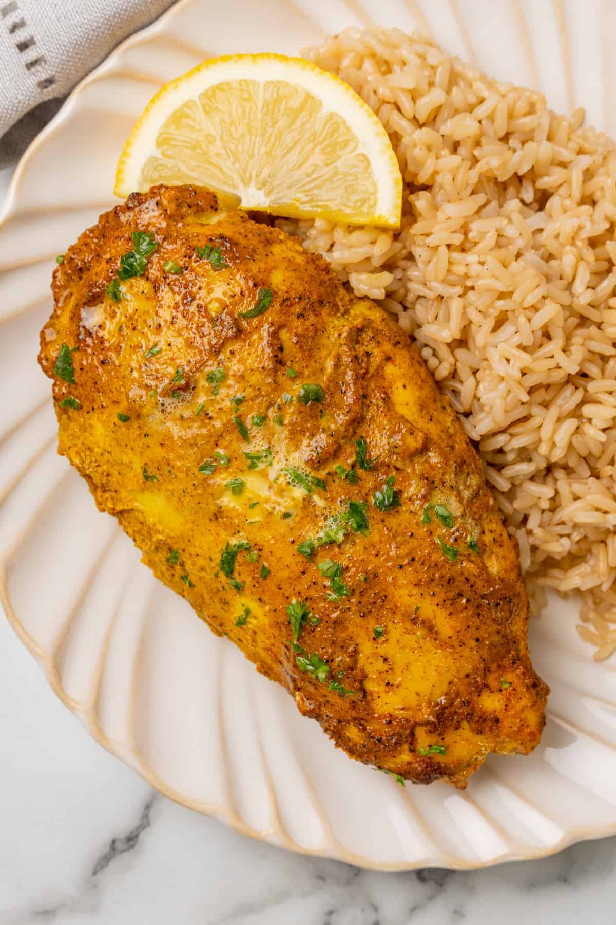 Tandoori Chicken with rice and a slice of fresh lemon on a white scalloped plate.