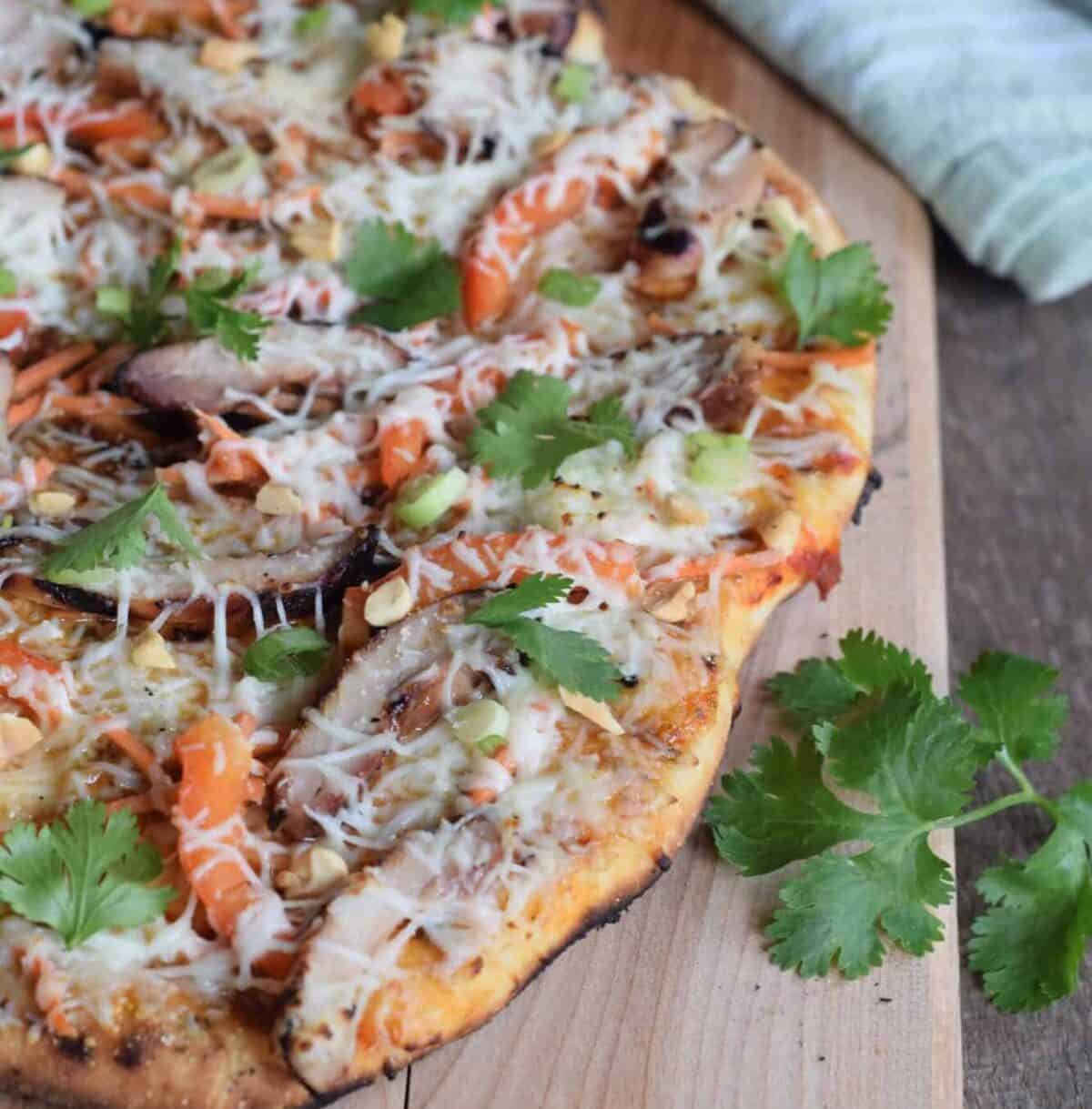 Shortcut Grilled Chicken Pizza made and sitting on a wooden cutting board with sprigs of fresh herbs.