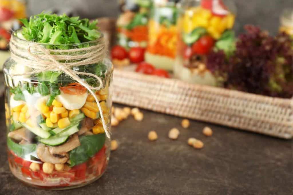 A mason jar salad filled to the top with more salads in the background