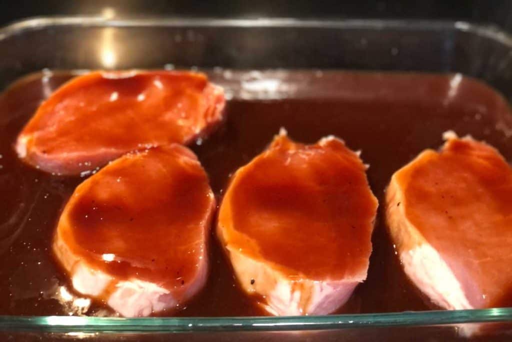Raw pork chops marinating and covered in bbq sauce in a glass dish