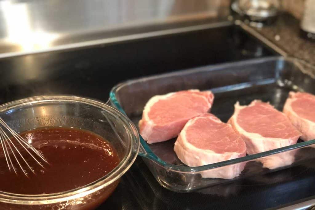 pork chops in a glass baking dish and a bowl full of bbq sauce with a whisk