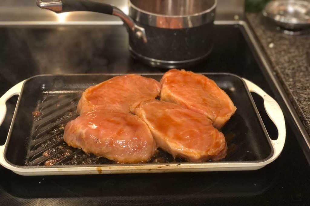 Boneless pork chops on a grill pan with a pot on the stove in the background