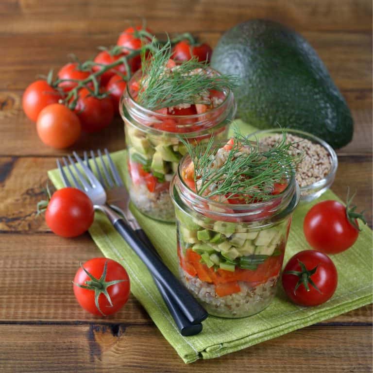 Mason jar salads with quinoa, tomatoes, avocados and tarragon on a green napkin with fresh tomatoes and avocados