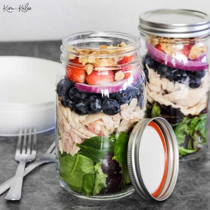 Strawberry Spiniach Salad in a jar in layers with lettuce, chicken, blueberries, red onion, strawberries and nuts.
