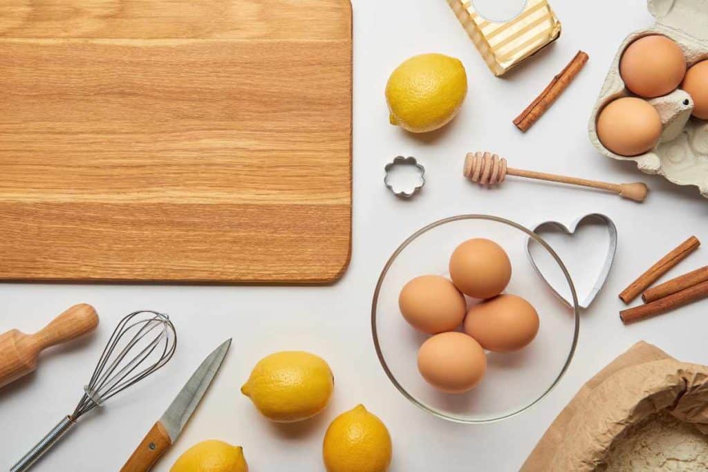 Baking supplies with a wooden cutting board, bowl of eggs, cookie cutters and lemons