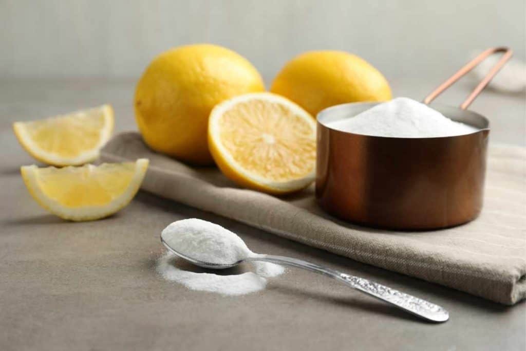 Measuring cup full of sugar with sliced lemons and a spoon on a linen napkin