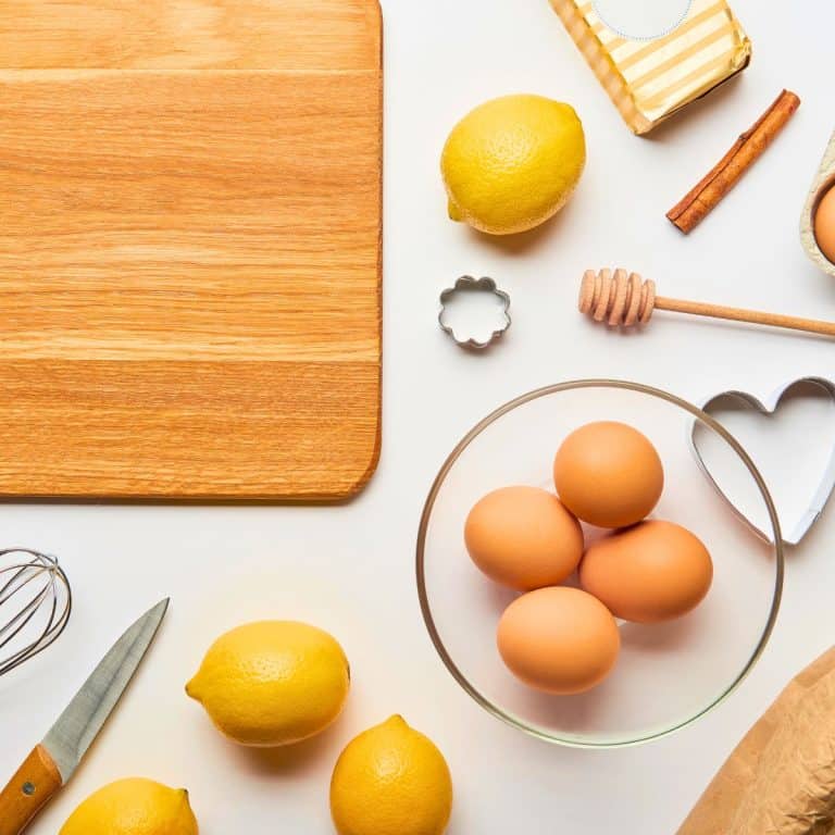 Baking supplies with a wooden cutting board, bowl of eggs, cookie cutters and lemons