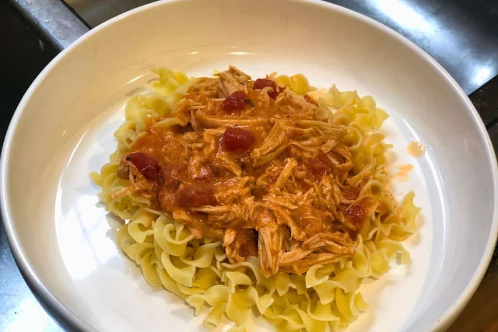 3-Jar Slow-Cooker Creamy Tomato Chicken served over egg noodles in a white bowl sitting on a wooden table
