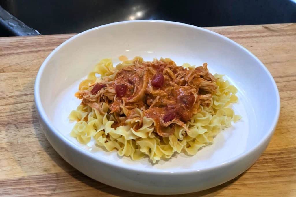 3-Jar Slow-Cooker Creamy Tomato Chicken served over egg noodles in a white bowl sitting on a wooden table