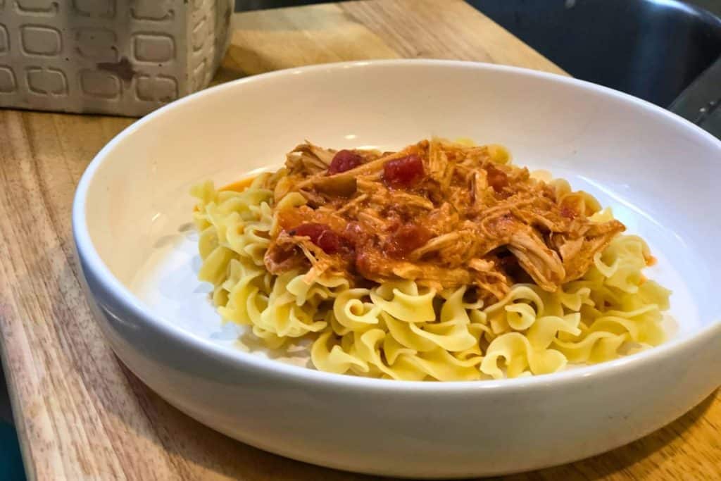 3-Jar Slow-Cooker Creamy Tomato Chicken served over egg noodles in a white bowl sitting on a wooden table
