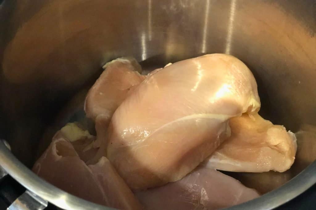 Raw chicken breasts sitting in the slow cooker during the assembly of ingredients for 3-Jar Slow-Cooker Creamy Tomato Chicken recipe