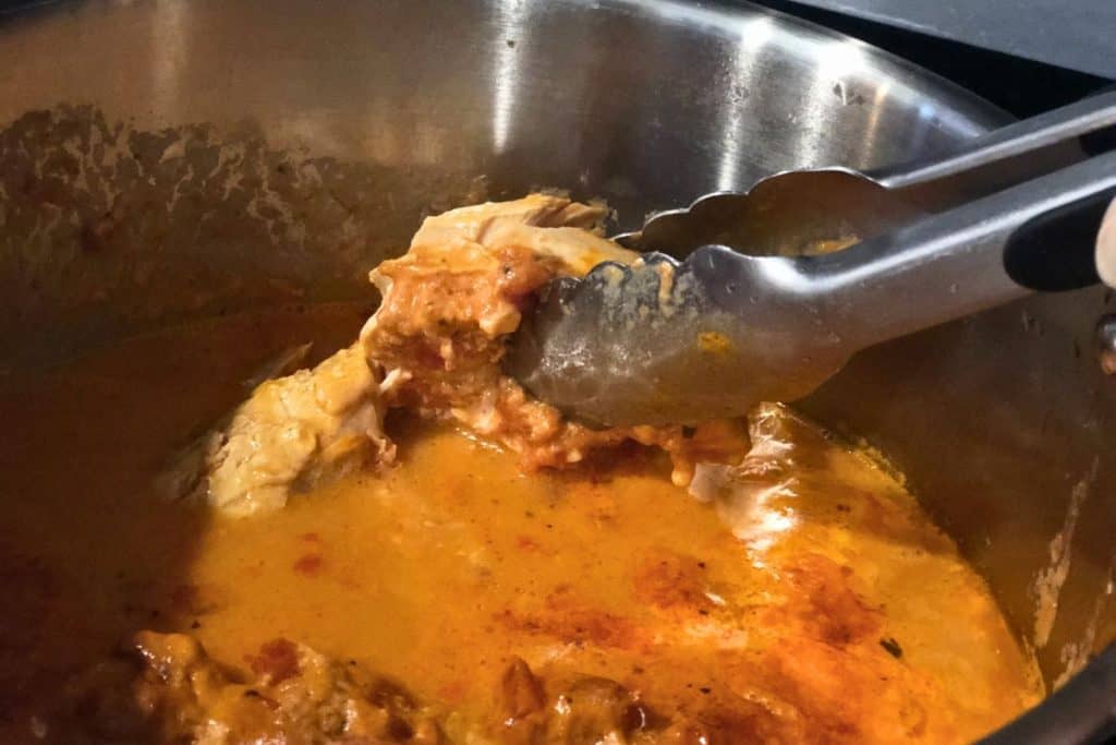 3-Jar Slow-Cooker Creamy Tomato Chicken that's finished cooking in the crock pot and falling into shredded pieces when picked up with tongs