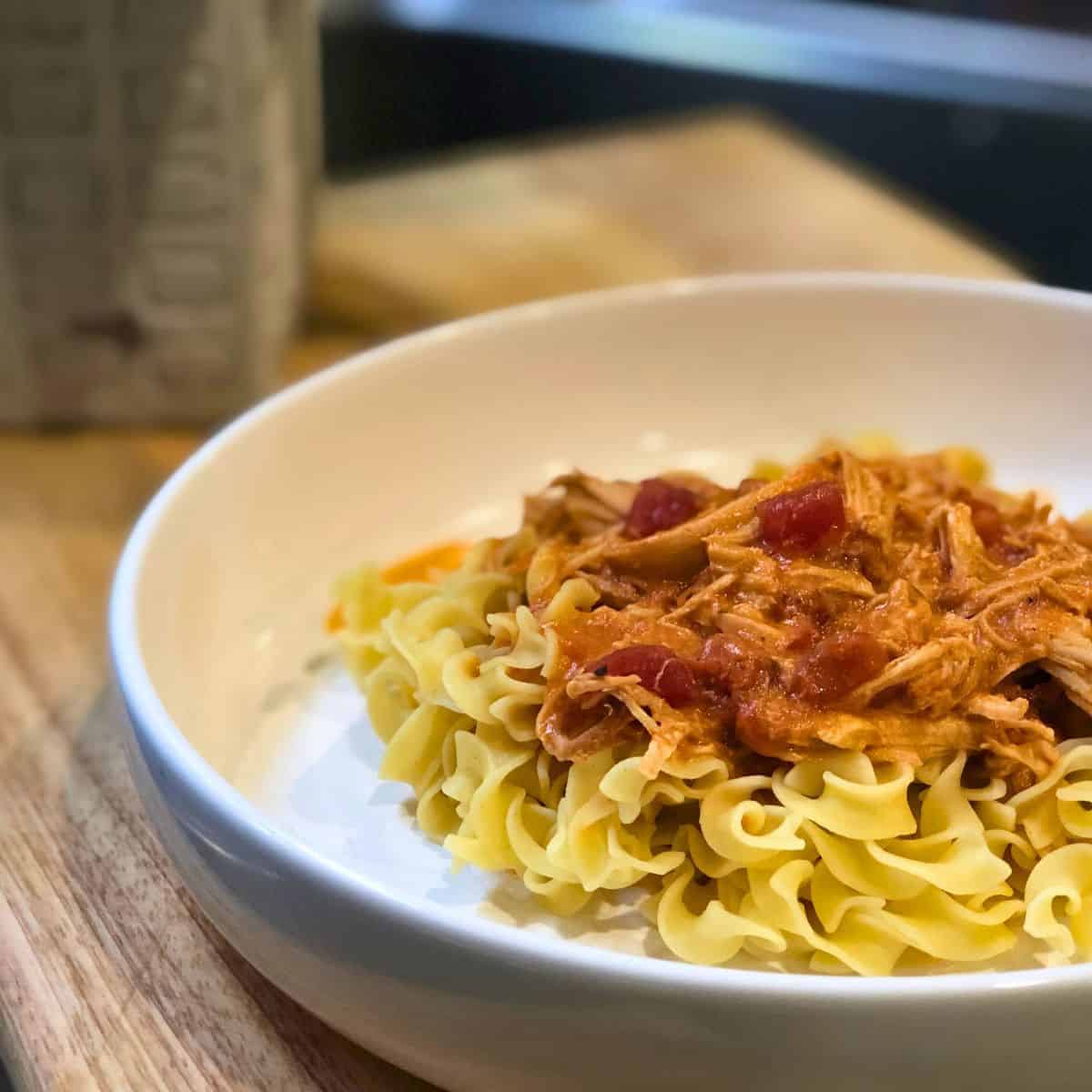 3-Jar Slow-Cooker Creamy Tomato Chicken served over egg noodles in a white bowl sitting on a wooden table