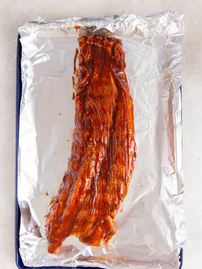 A rack of ribs that has been brushed with bbq sauce and is ready to go under the broiler.