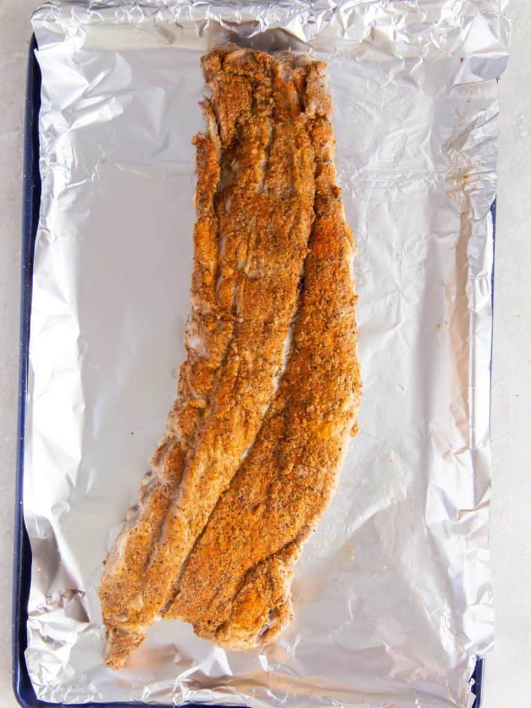 Cooked baby back ribs with dry rub on a foil lined baking sheet