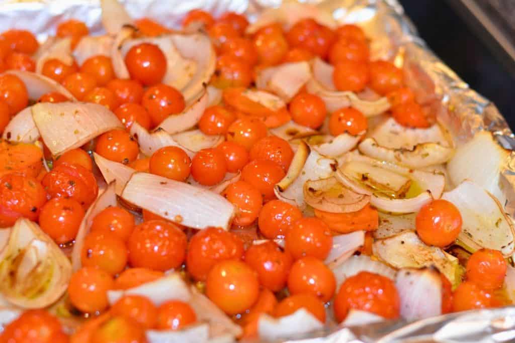Roasted tomatoes, onions and carrots on a foil-lined baking sheet, halfway through the roasting time.