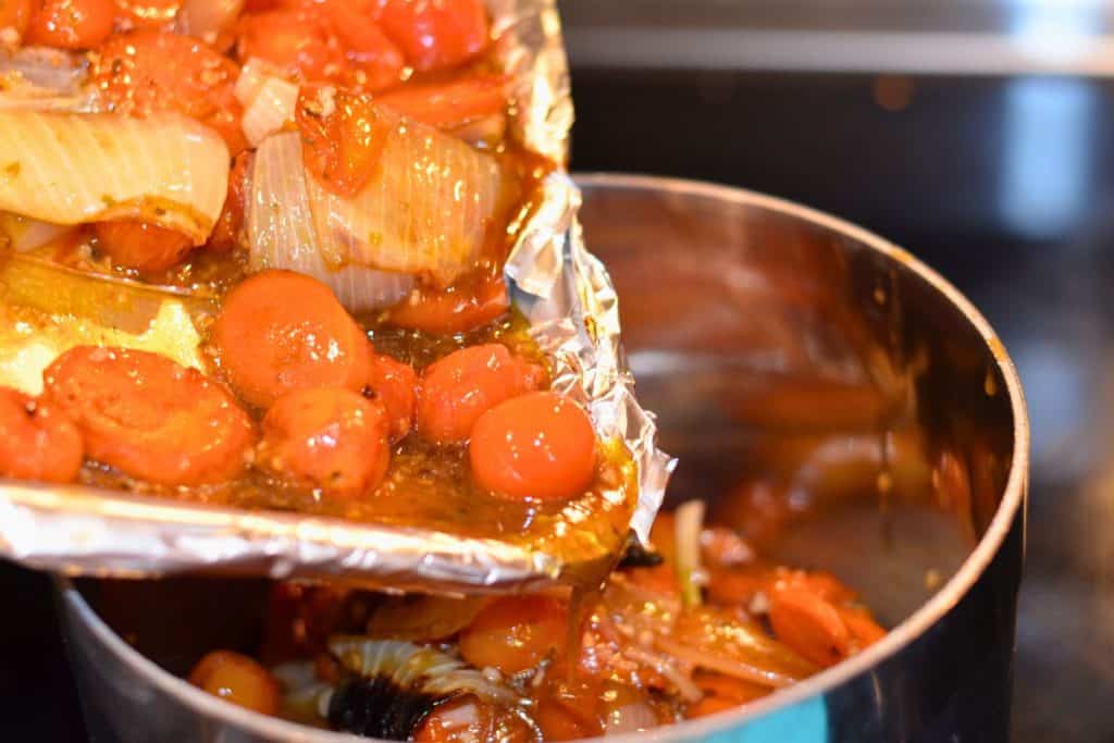 Pouring all the roasted vegetables and their roasting juices from the foil lined pan into a heavy bottomed sauce pan.